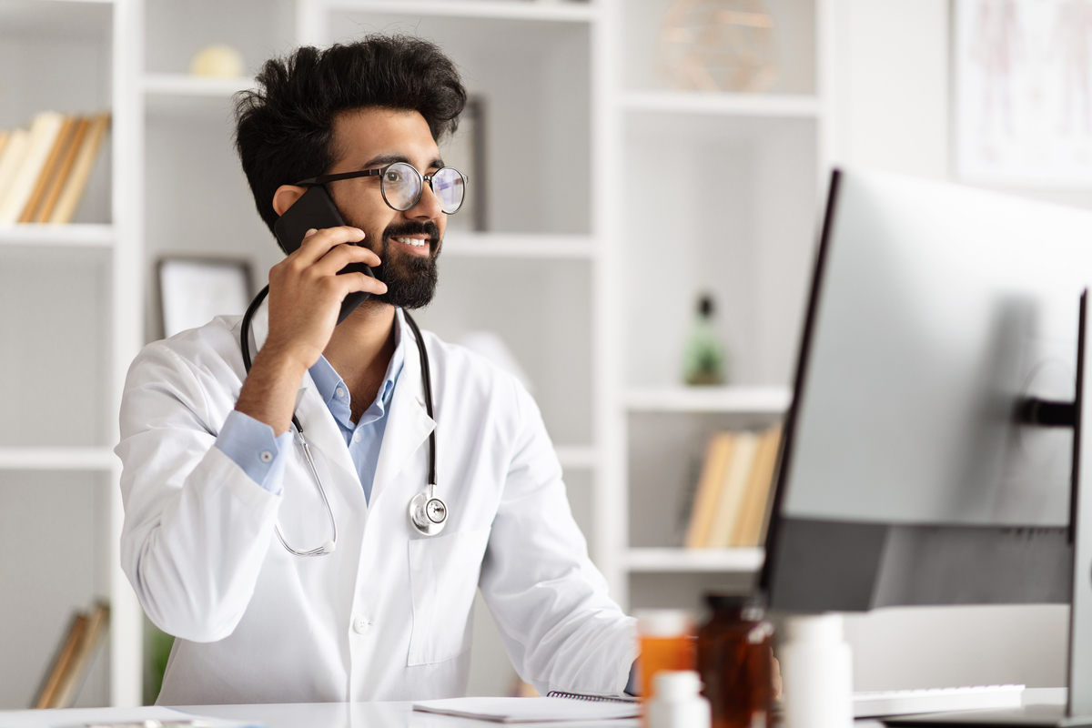 Médico fazendo multitarefa com computador e telefone na clínica