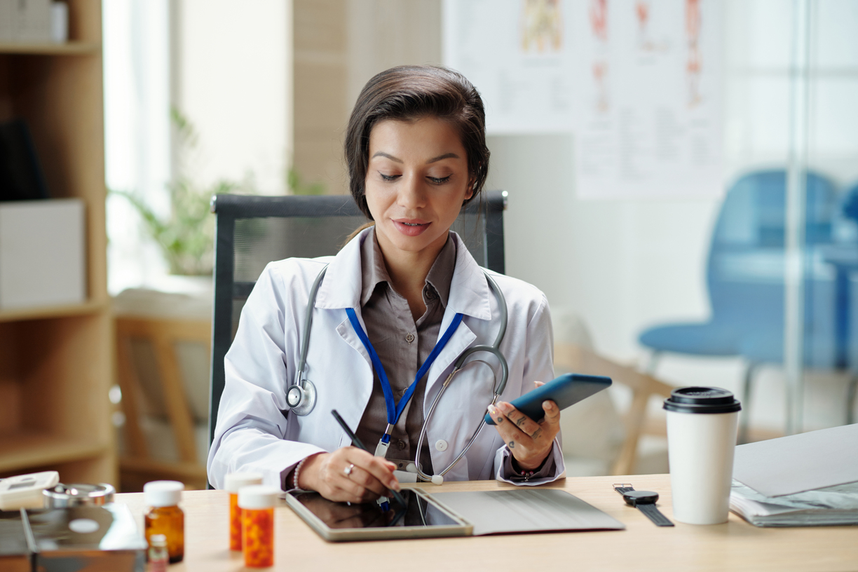 Médica da clínica médica verificando o smartphone e fazendo anotações na plataforma de gestao